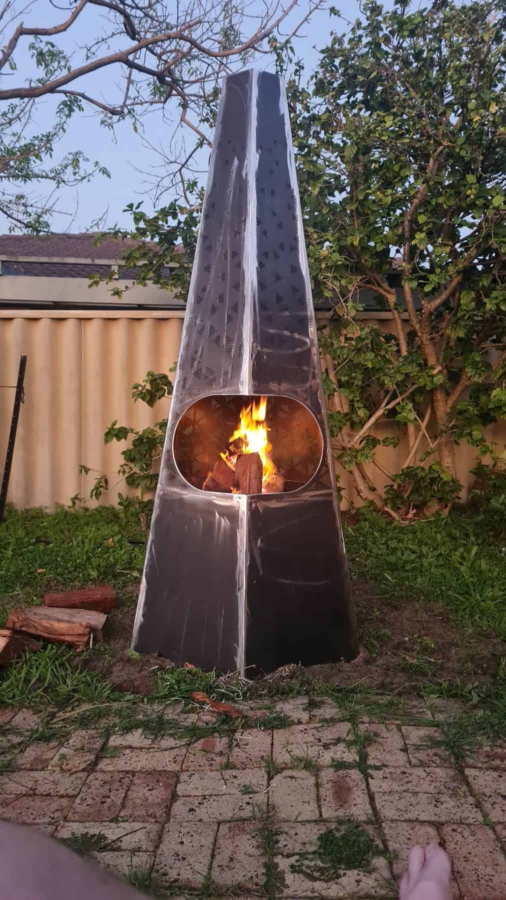 Metal fire pit in sunny outdoor setting, fire illuminating perforated pattern