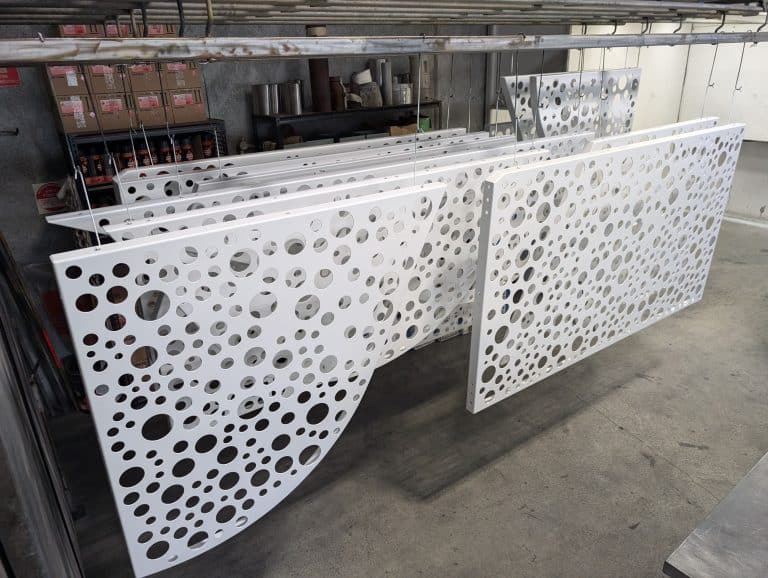 Finished architectural metal screens with custom turret-punched designs, powder coated in white and ready for installation.